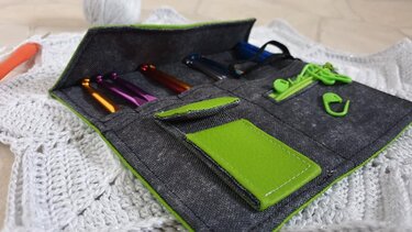 Graues Häkelnadeln-Etui mit grünen Einsätzen, offen mit bunten Häkelnadeln und Maschenmarkierern