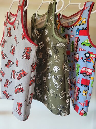 Drei ärmellose Kindershirts: grau mit Feuerwehrautos, olivgrün mit Grafikprints und hellblau mit bunten Fahrzeugen, hängend an weißen Bügeln.