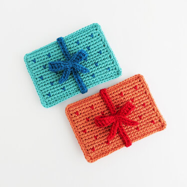 Zwei gehäkelte Mini-Geschenke in Türkis und Orange mit Herzmotiven und Schleifen auf weißem Hintergrund.