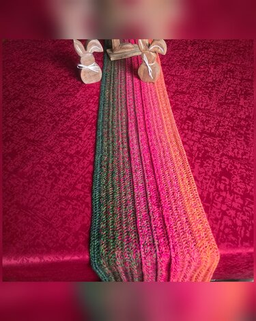 Gehäkelter mehrfarbiger Tischläufer (Grün–Orange–Pink) auf roter Tischdecke mit zwei Holzhasen