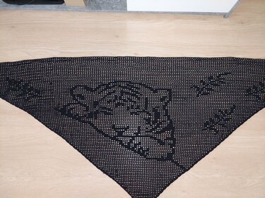 Schwarzes gehäkeltes Dreieckstuch mit Tigerkopf‑Motiv auf hellem Boden