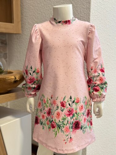 Hellrosa Langarm-Kinderkleid mit Rosenbordüre an Saum, Ärmeln und Stehkragen, auf einer Schneiderpuppe.