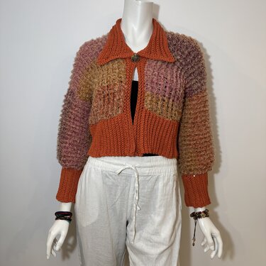 Cropped open-front crochet cardigan with orange, pink and brown patchwork panels on a mannequin.