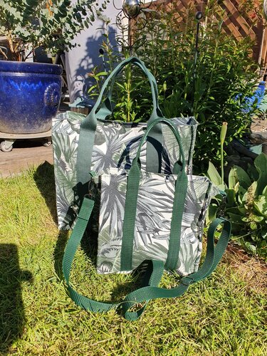 Zwei grüne Stofftaschen mit Blattmuster und dunkelgrünen Tragegurten auf Gras