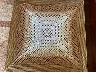 Quadratisches hellbeiges gehäkeltes Deckchen mit Filetmuster auf geflochtener Oberfläche