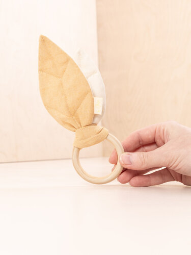 Wooden ring teether with knotted yellow and cream fabric ears held by hand