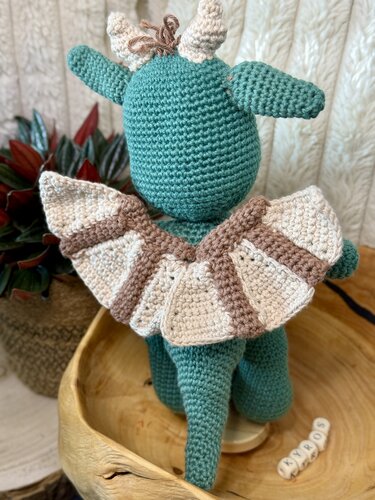Gehäkelter petrolfarbener Amigurumi-Drache von hinten mit beiger-brauner Rüschenhalskrause und kleinen Hörnern