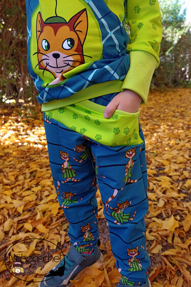 Nahaufnahme einer Kinderhose mit Katzenmotiv, Eingrifftasche und Bündchen, Kind steht im Laub