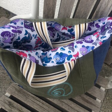 Olivgrüne Stoff-Einkaufstasche mit gestreiften Trägern und weißem Innenfutter mit bunten Cartoon-Fischen