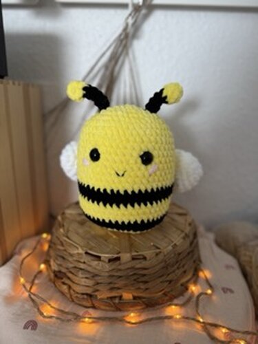 Gehäkelte Amigurumi-Biene in Gelb und Schwarz mit weißen Flügeln auf geflochtenem Korb und Lichterkette