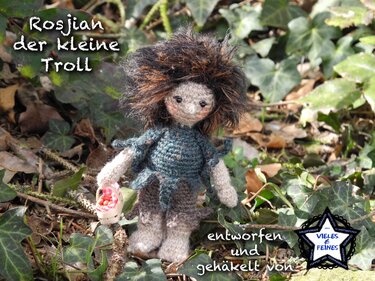 Nahaufnahme einer gehäkelten Amigurumi-Puppe: kleiner Troll mit braunem, wuscheligem Haar, türkisfarbenem Oberteil und Mini-Korb vor Efeu.