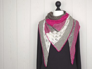 knitted triangle shawl with garter stripes, eyelet lace panels and pink edging draped on a mannequin