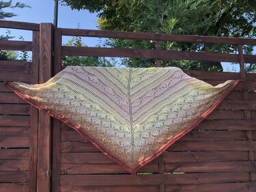 Gestricktes Dreieckstuch in Gelb-, Rosa- und Burgundertönen mit Lochmuster, über einem Holzzaun drapiert