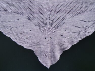 Light purple triangular lace shawl with a stylized face and heart motif on a dark background.