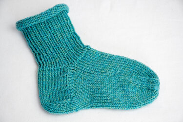 Türkisfarbene gestrickte Socke auf hellem Hintergrund mit sichtbarem Rippenbündchen.
