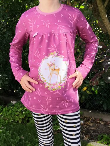 Kind trägt pinkes Langarmshirt mit Rehkitz in einem Blumenkranz sowie dezentem Blatt- und Punktmuster.