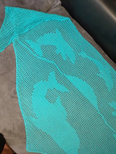 Türkises gehäkeltes Tuch mit offenem Netz und angedeuteten Fischmotiven auf dunklem Untergrund