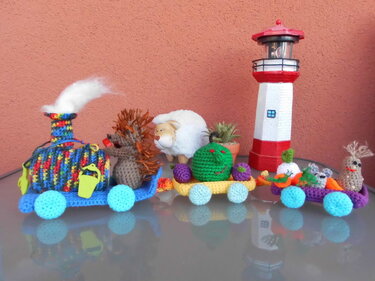 Gehäkelter Amigurumi-Zug mit Igel, Schaf und Gemüse auf glänzender Fläche vor roter Wand