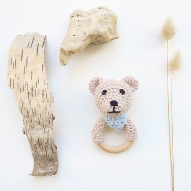 Gehäkelter Bärenkopf mit hellblauem Halstuch an rundem Holzgreifring auf weißem Hintergrund