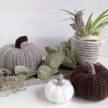 Small white, medium gray, and large brown crocheted pumpkins with eucalyptus and a textured pot