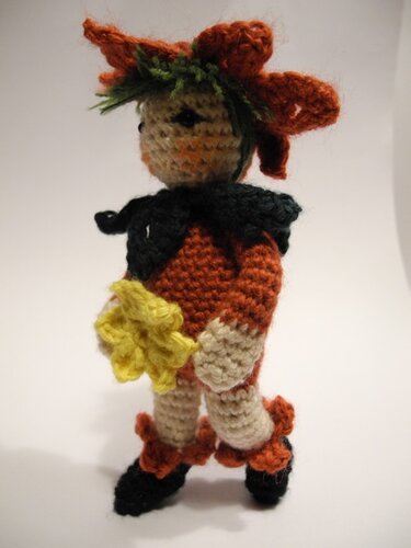 Gehäkelte Amigurumi-Puppe in orangefarbenem Outfit mit grünem Haar, dunklem Kragen und gelber Blume