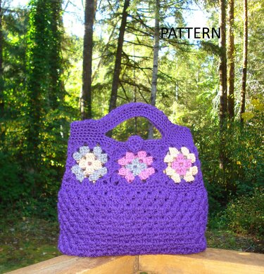 Close-up of a purple crochet clutch showing granny-square flower inserts, built-in handle and loop closure, against a forest background