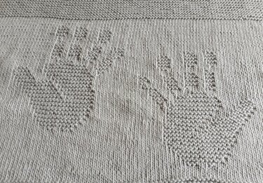 Hellgraue gestrickte Decke mit zwei eingestrickten Handmotiven