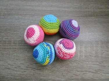 Fünf kleine, schnell gehäkelte Kugeln in verschiedenen Farben auf Holz
