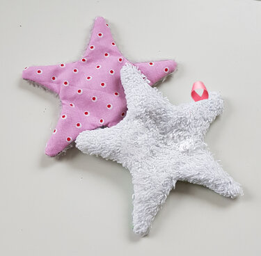 Zwei genähte Stoffsterne: weißer Frottee-Stern mit rosa Schlaufe und rosa Baumwollstern mit roten Punkten