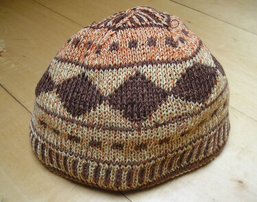 Gestrickte Mütze in Brauntönen mit mehrfarbigem Muster auf Holz