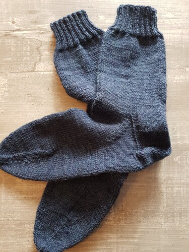 Dunkelgraue, glatt-rechts gestrickte Herrensocken mit Rippenbündchen auf Holzuntergrund