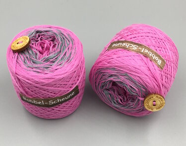 Zwei pink-graue Bobbel-Garne mit Holzknöpfen auf grauem Hintergrund