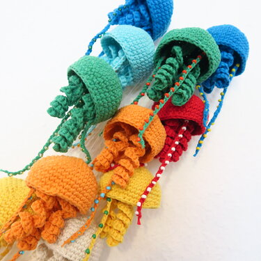 Bunte handgehäkelte Amigurumi-Quallen mit perlenverzierten Tentakeln auf hellem Hintergrund