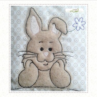 Stickerei eines beigen, flauschigen Hasen mit lila Blume auf hellem Stoff