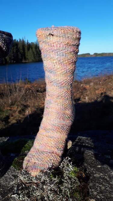 Pastellfarbener handgestrickter Kniestrumpf auf einem Felsen vor einem See