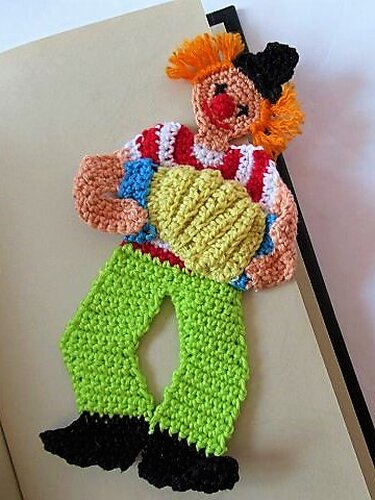 Gehäkeltes Clown-Lesezeichen mit orangefarbenen Haaren, roter Nase, gestreiftem Oberteil und grüner Hose.