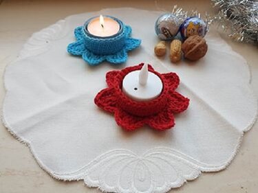 Zwei gehäkelte Blüten-Teelichthalter in Rot und Blau auf weißem Deckchen