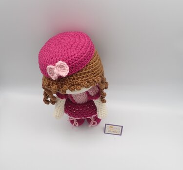 Crocheted amigurumi doll with pink beret, curly brown hair, and textured skirt viewed from an elevated angle