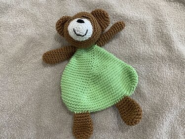 Gehäkeltes Bären‑Schmusetuch mit hellgrünem Körper auf hellbeigem Handtuch