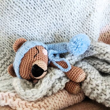 Gehäkelter brauner Teddybär mit blauer Bommel-Schlafmütze auf gestrickten Decken
