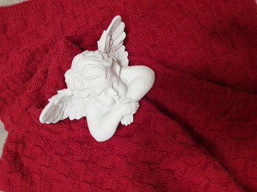 Rote gestrickte Decke mit geometrischem Zopfmuster und weißer Engelfigur