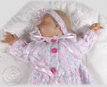Gestrickte Babyjacke mit Blütenknöpfen, Satinbändern und Stirnband auf Babypuppe