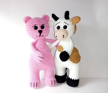 Rosafarbener Amigurumi-Bär neben gefleckter Amigurumi-Kuh