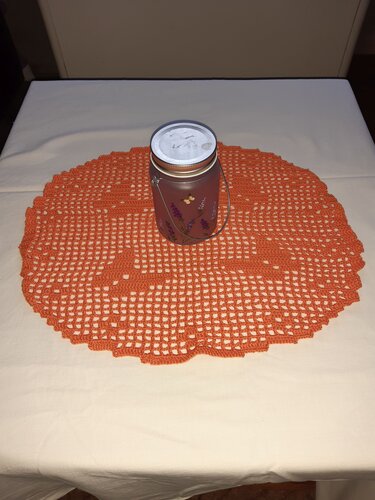 Oranges rundes gehäkeltes Deckchen auf hellem Tisch mit Laterne