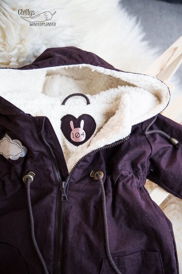 Detailaufnahme: Herz‑Häschen‑Plott auf innenliegendem Teddyfutter einer dunkellila Jacke