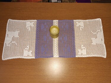 Gehäkelter Filet-Tischläufer mit weißen Motivfeldern und lilafarbenem Mittelteil, Kerze auf Holztisch