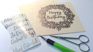 Gebastelte Geburtstagskarte mit floralem Kranz-Plott 'Happy Birthday', Transferfolie mit deutschen Schriftzügen, Schere und Präzisionsmesser