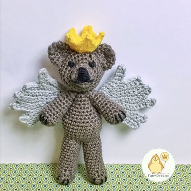 Gehäkelter brauner Teddybär mit hellgrauen Flügeln und gelber Krone