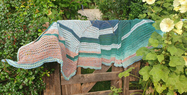 Gestreiftes halbrundes Häkel-Tuch mit offenem Lochmuster und gezacktem Rand über einem Holztor