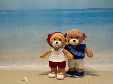 Zwei gehäkelte Amigurumi-Teddybären in Sommeroutfits vor Strandhintergrund